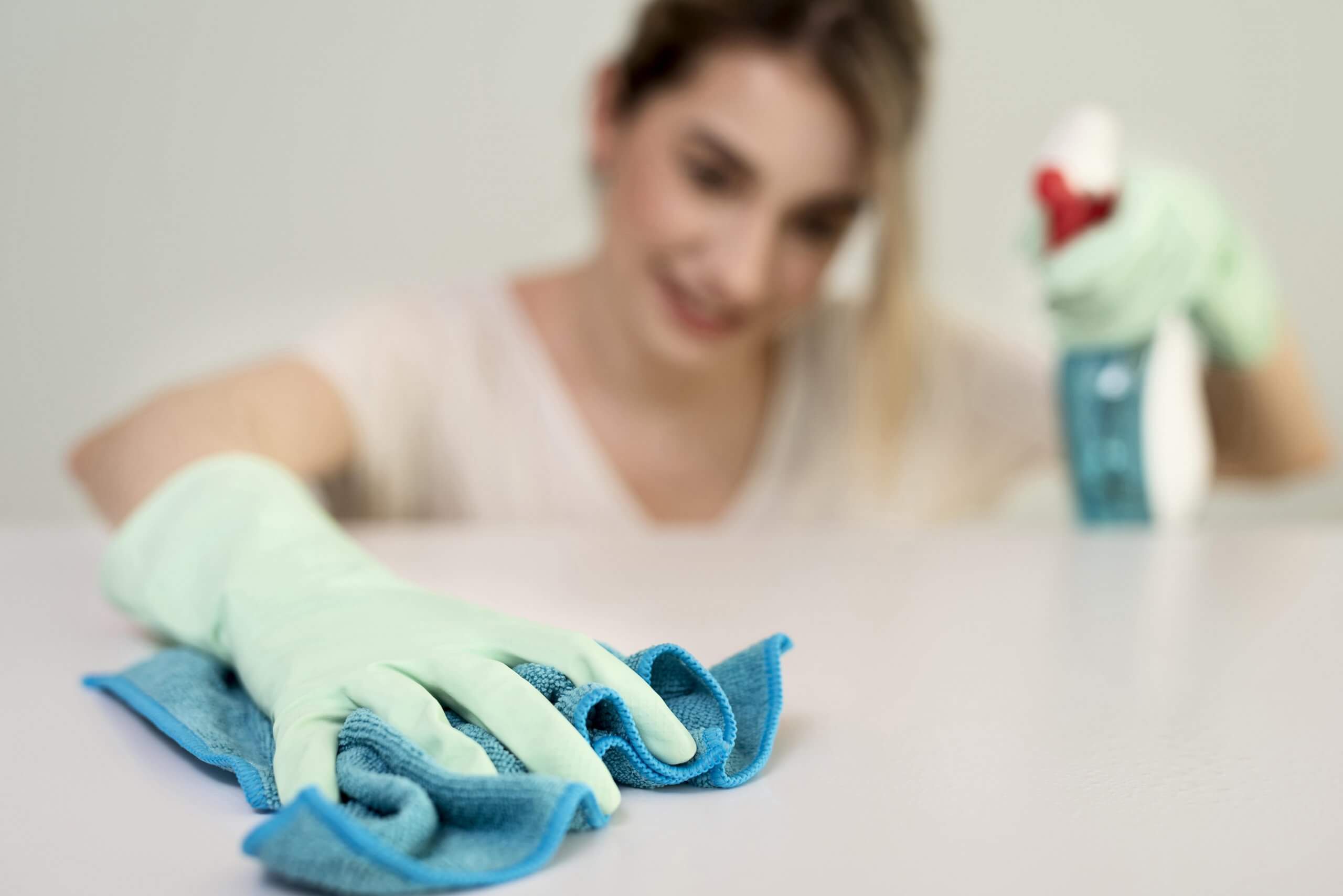 mulher a limpar uma superfície com pano e produto de limpeza a usar luvas