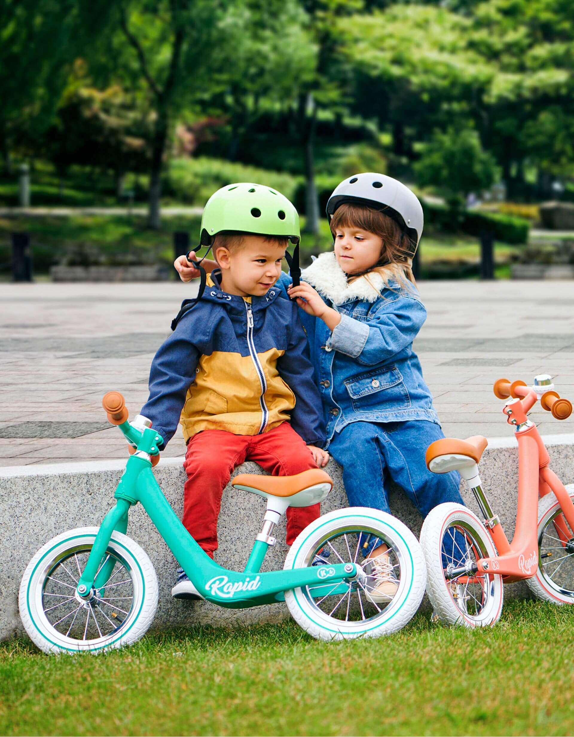 duas crianças sentadas num banco com bicicletas e capacetes